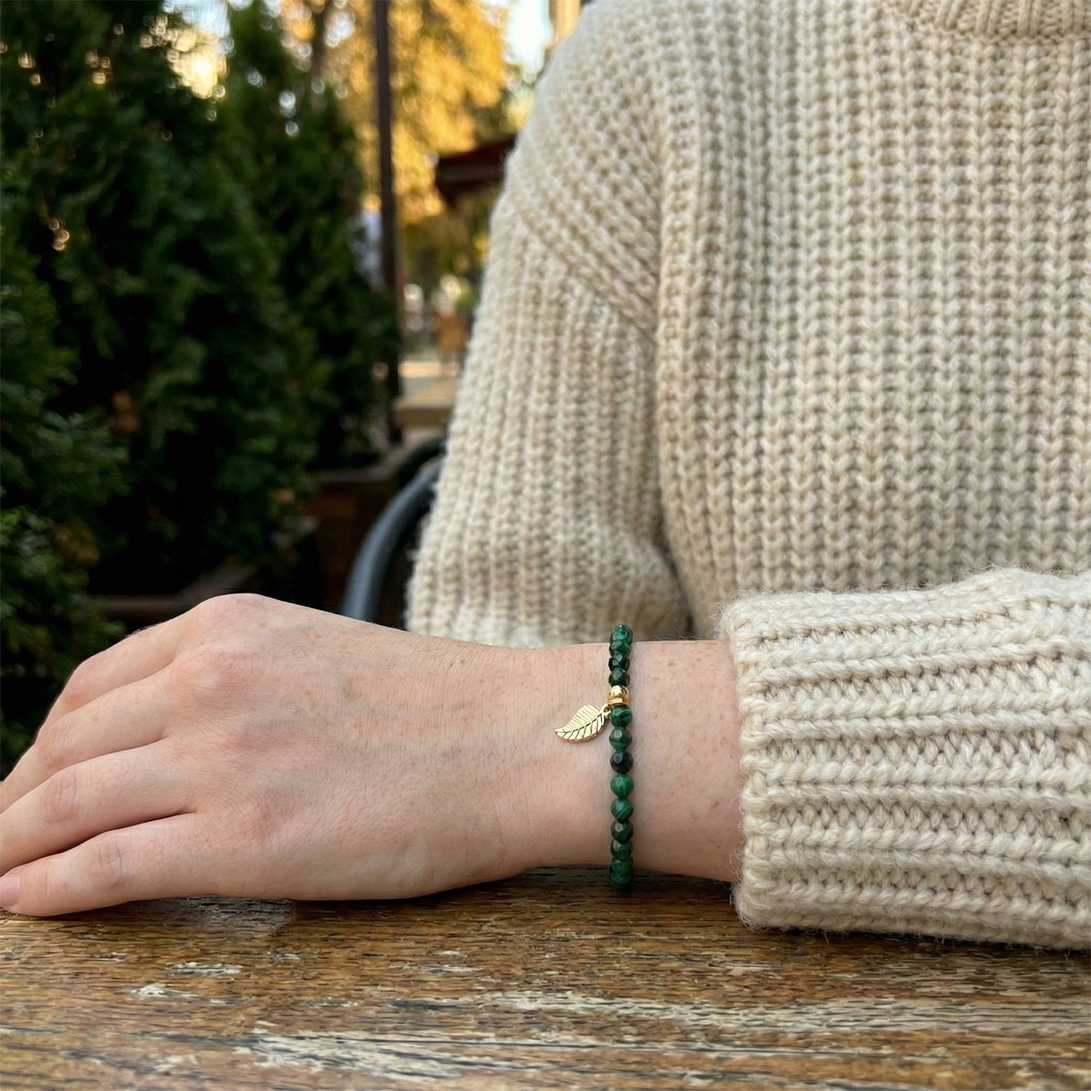 Person wearing a green bracelet on a wooden surface with a blurred natural background