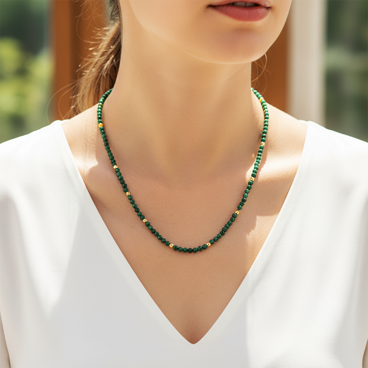 Green beaded necklace worn by a person in a white top with a blurred background