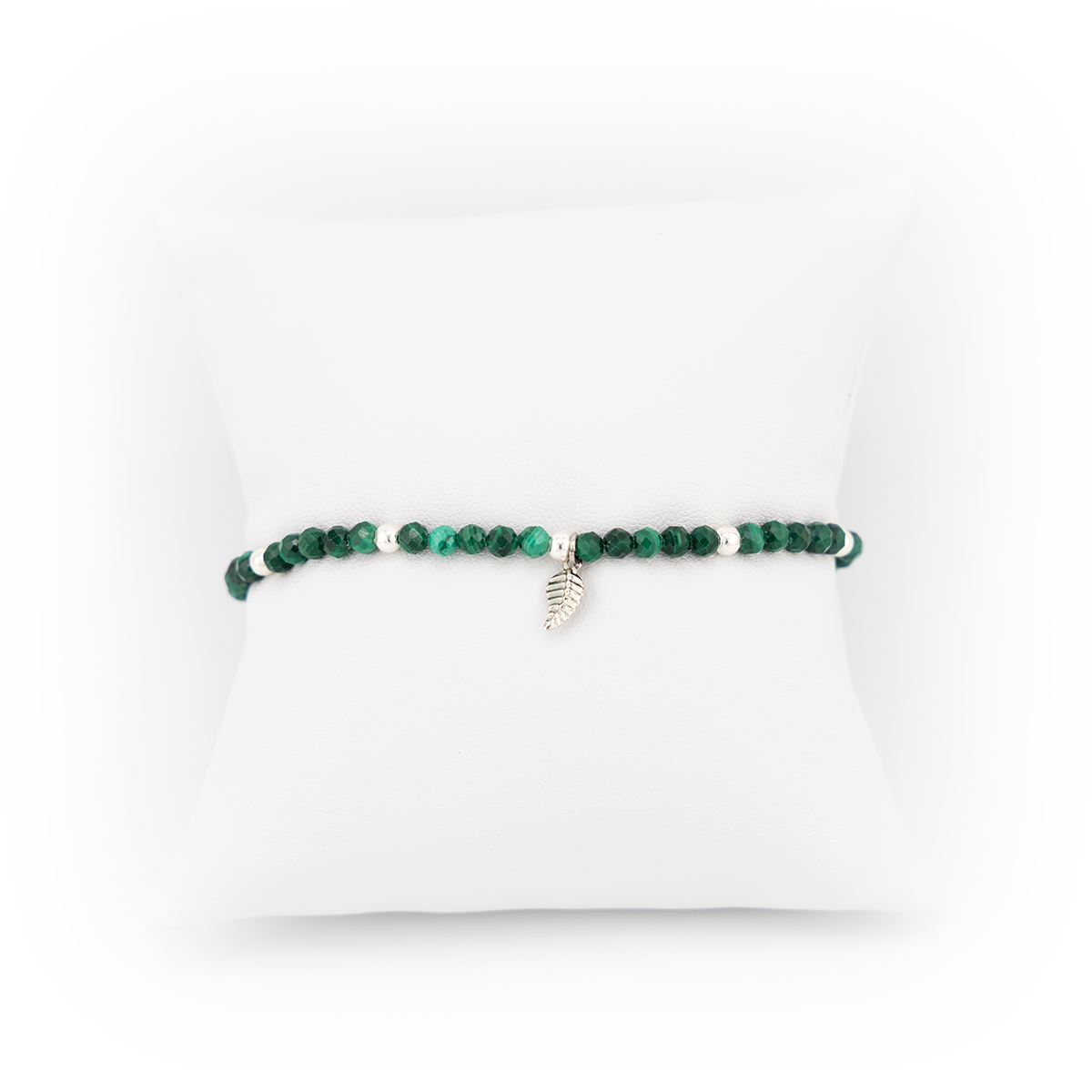 Green beaded bracelet with a silver charm on a white pillow