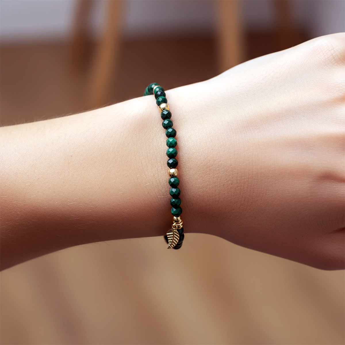Green beaded bracelet with a leaf charm on a wrist against a blurred background