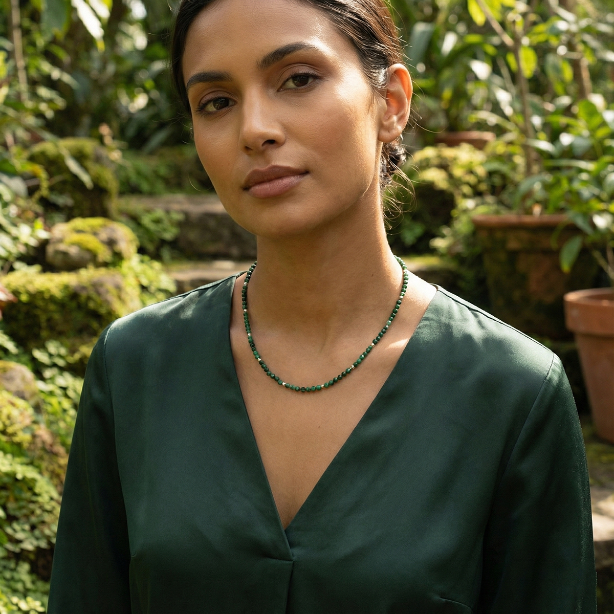 Woman wearing a green top and necklace in a garden setting