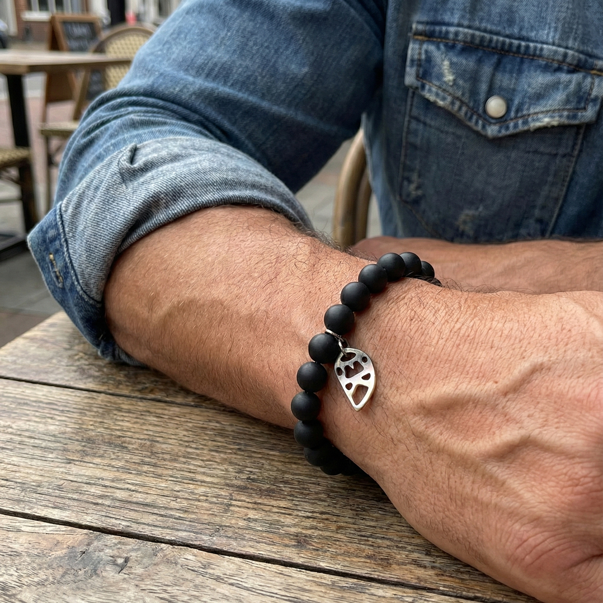 Person wearing a black beaded bracelet with a silver heart charm on a wooden table.