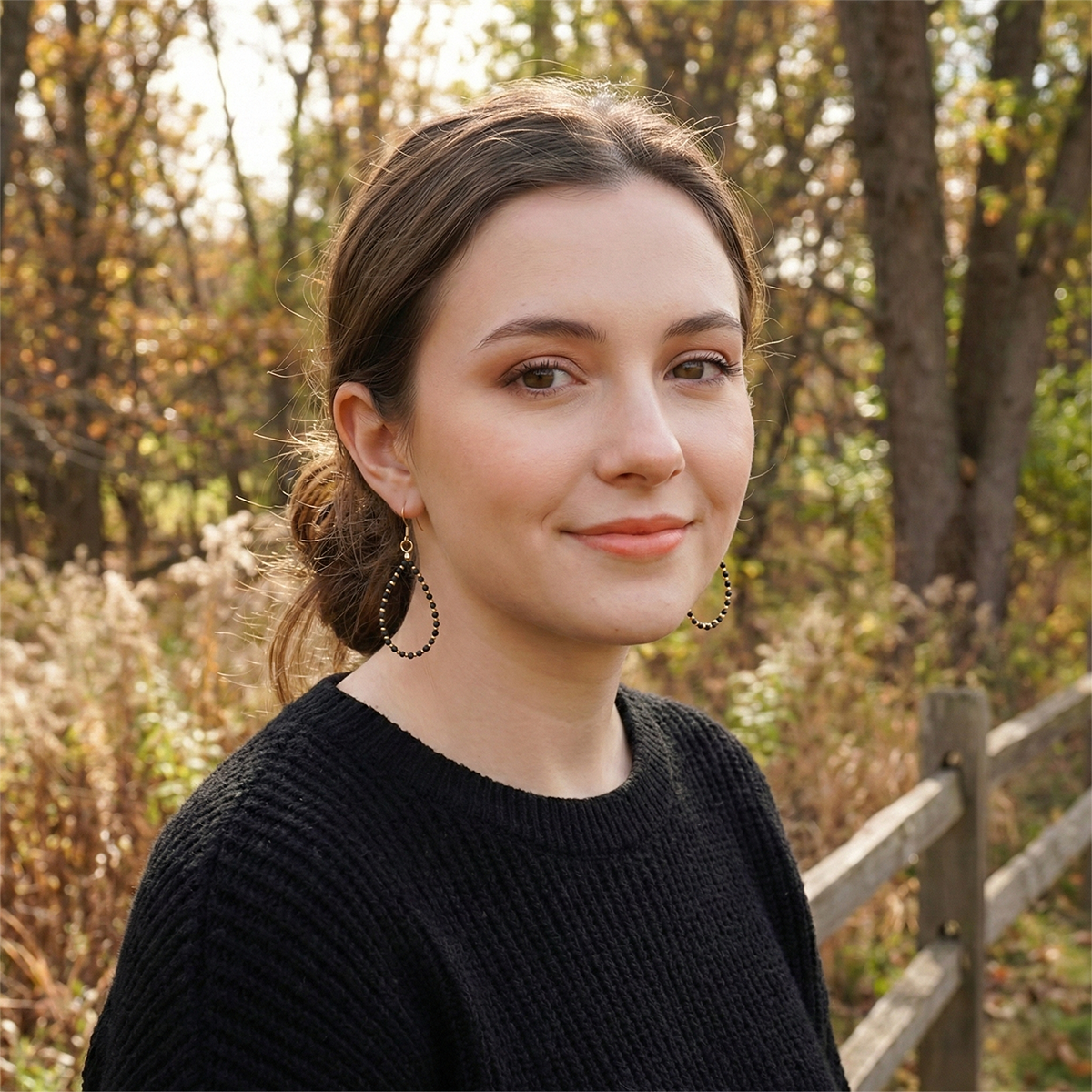 Woman standing in a forest with trees and a wooden fence in the background