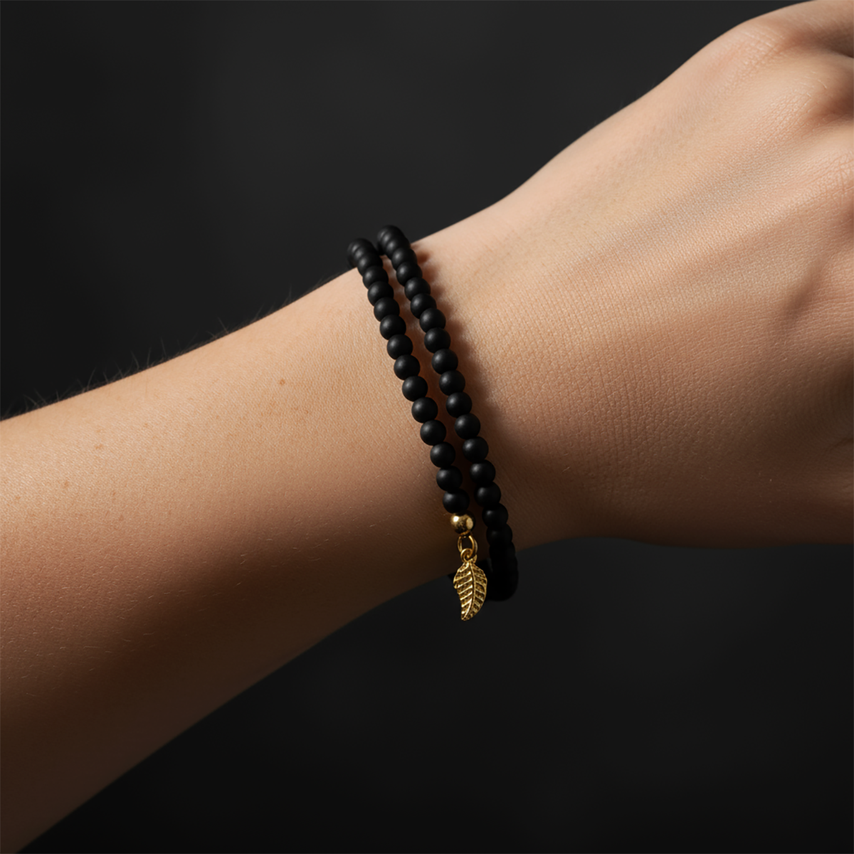 Black beaded bracelet with a gold leaf charm on a wrist against a dark background