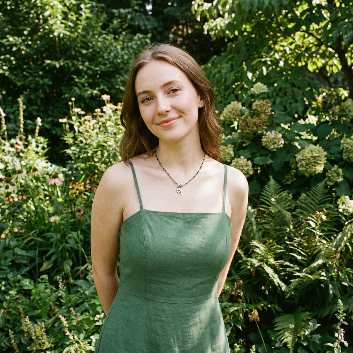 Woman in a green dress standing in a garden with greenery and flowers around her.