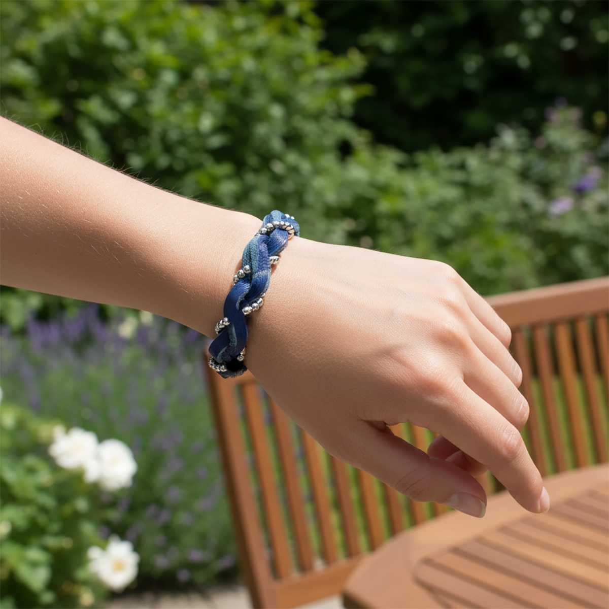 Person wearing a blue braided bracelet outdoors with greenery and flowers in the background