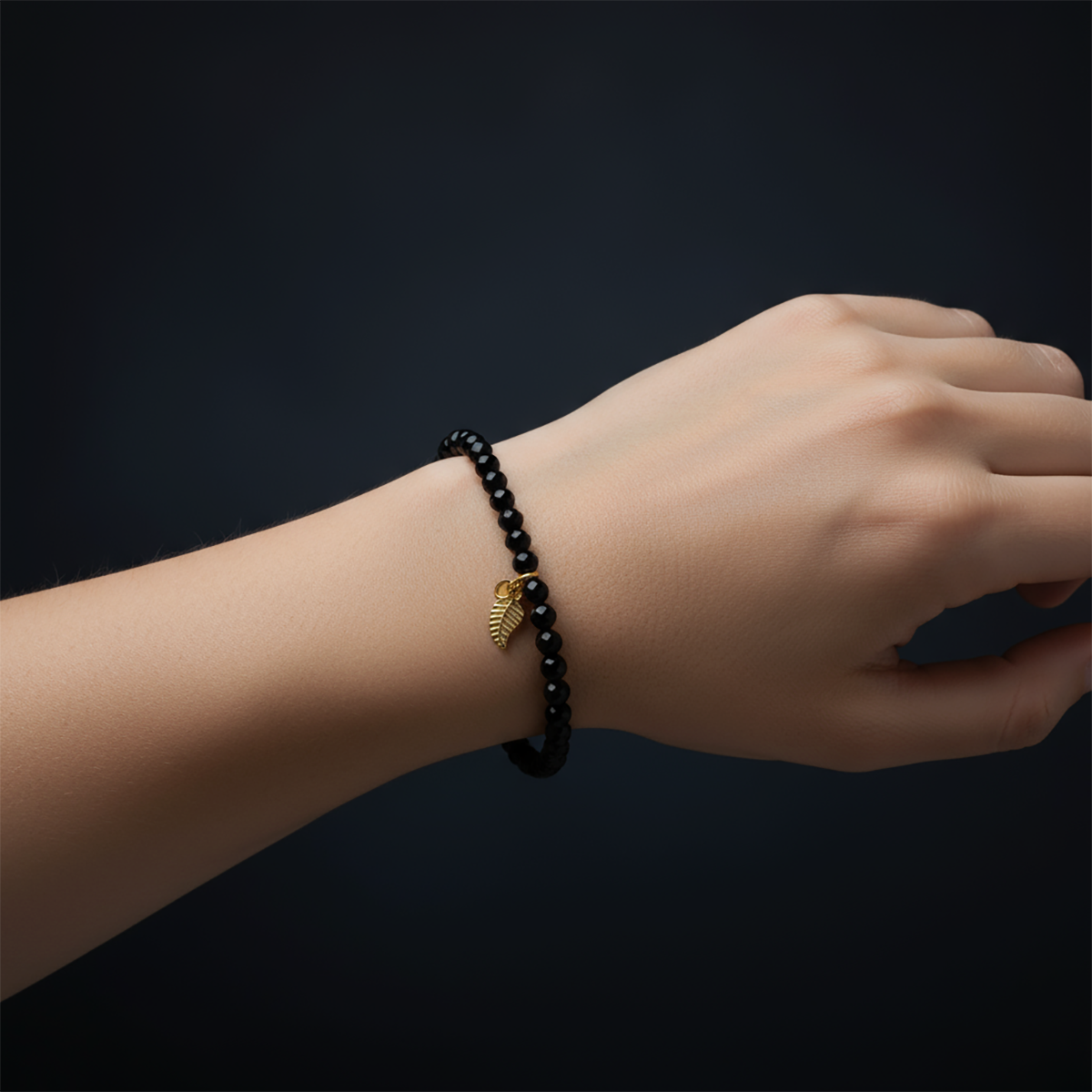 Hand wearing a black beaded bracelet with a gold charm on a dark background