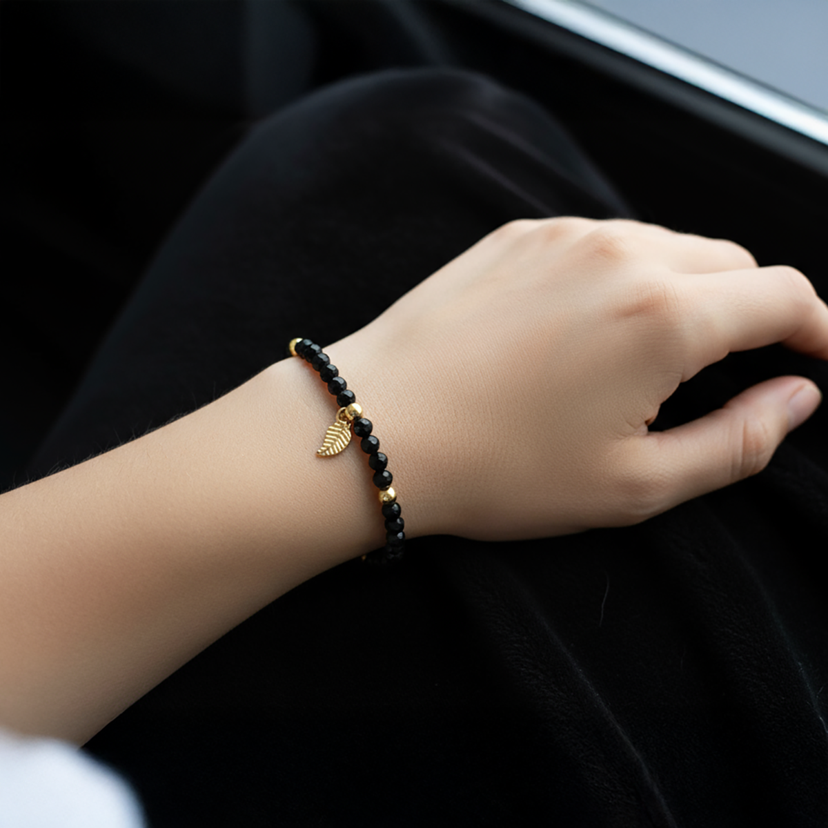 Hand wearing a black beaded bracelet with a gold charm on a dark background