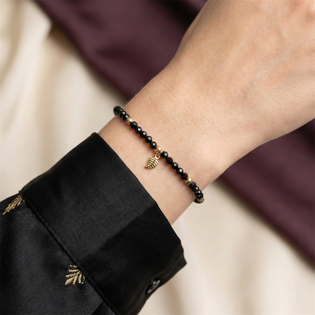 Black beaded bracelet with gold charms on a wrist against a neutral background