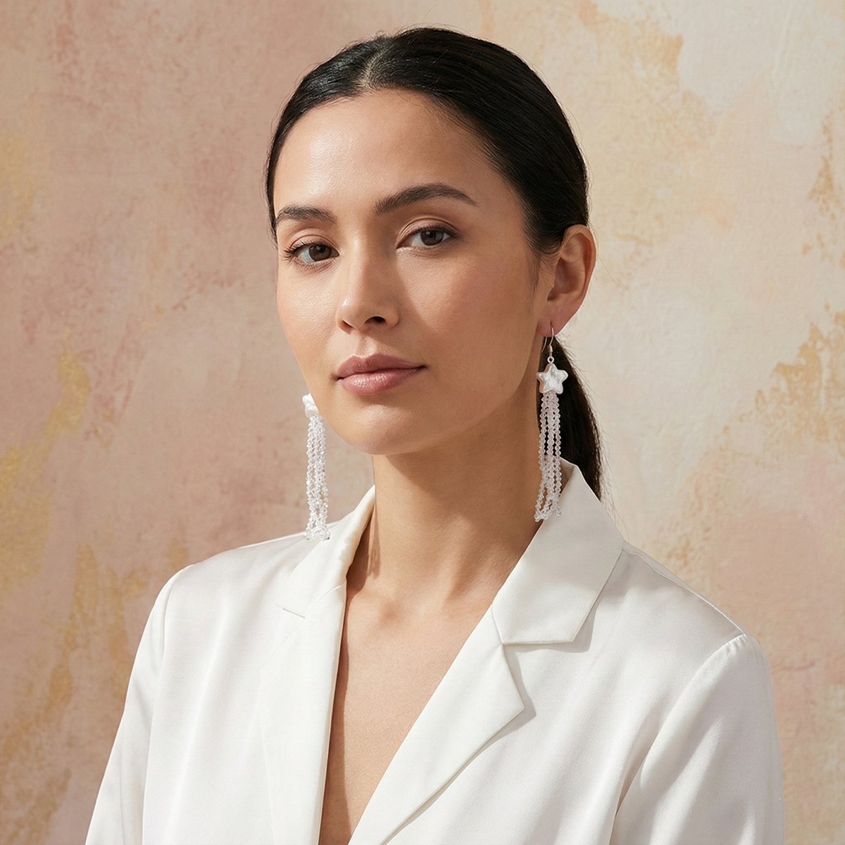 Woman wearing a white blazer with long earrings against a beige background