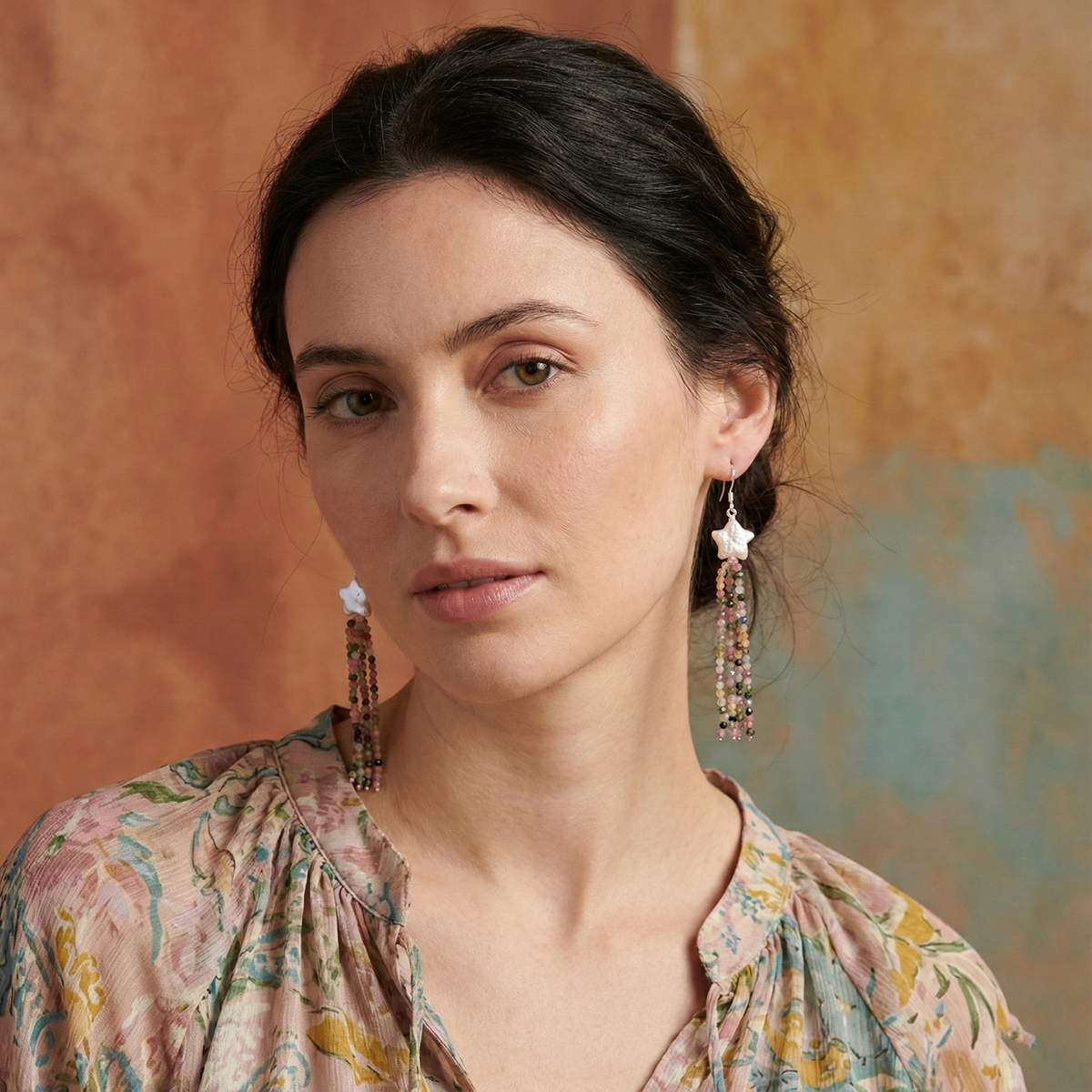 Woman wearing floral earrings against a textured wall.