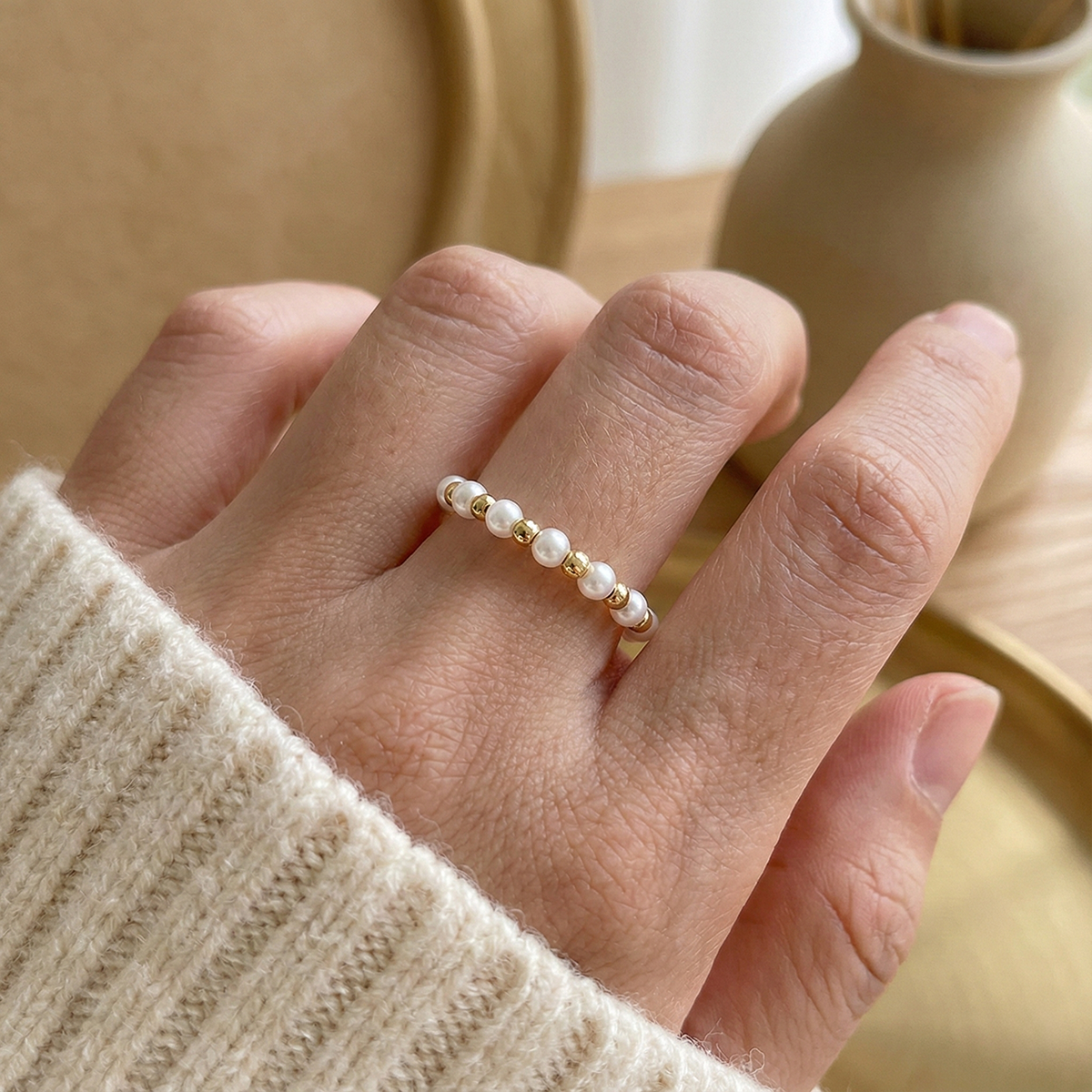 Hand wearing a pearl ring with a neutral background