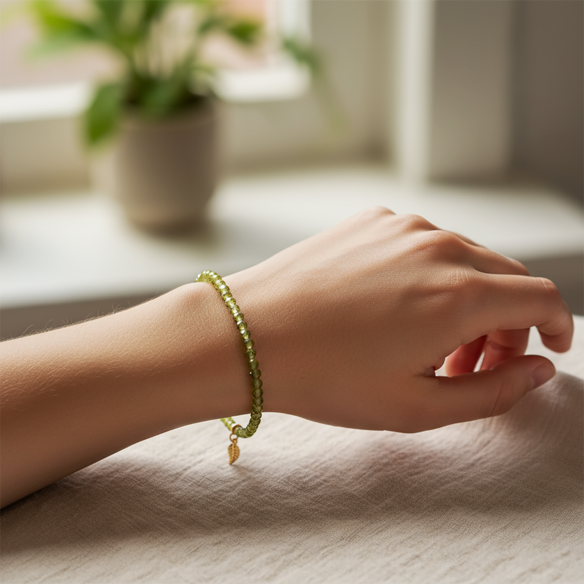 Hand wearing a green beaded bracelet with a blurred indoor background