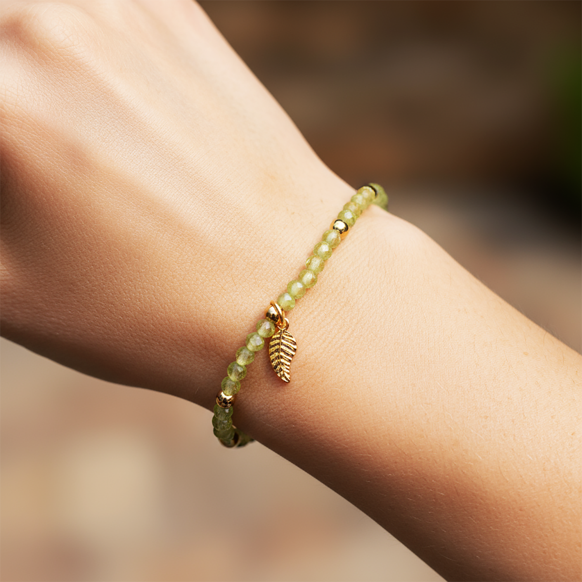 Green beaded bracelet with a leaf charm on a wrist against a blurred natural background