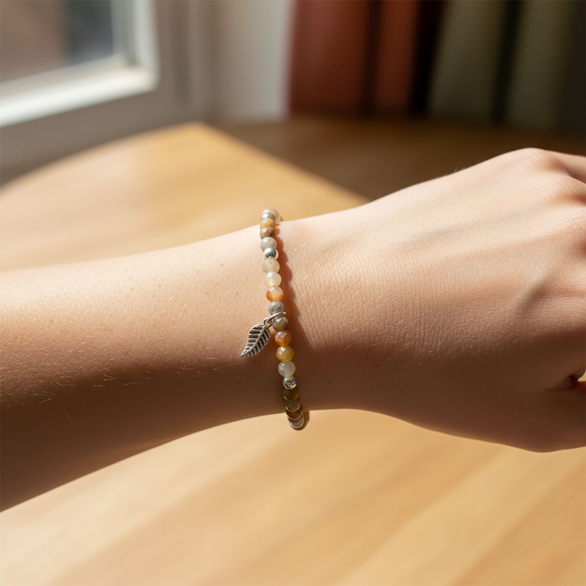 Close-up of a wrist wearing a beaded bracelet with a leaf charm, sunlight casting shadows.