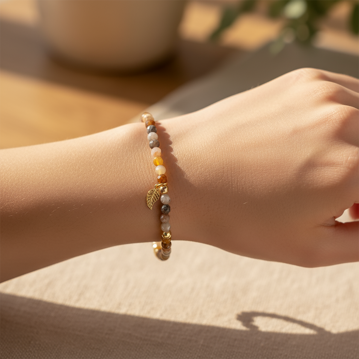 Hand wearing a beaded bracelet with a leaf charm on a neutral background