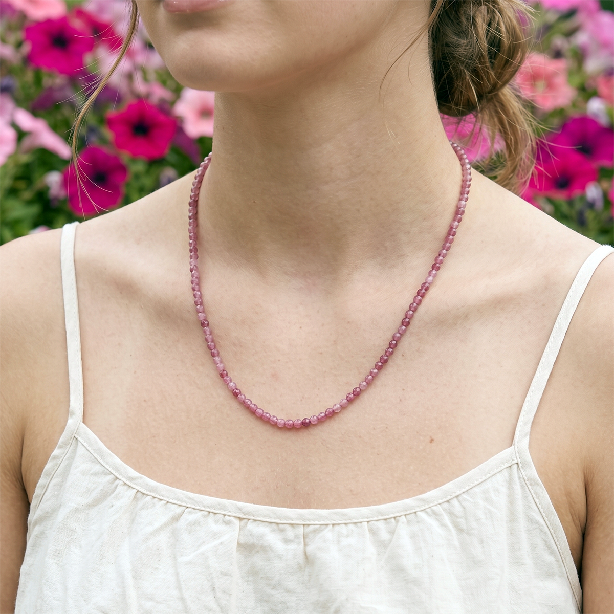 Woman wearing a pink beaded necklace with a blurred floral background