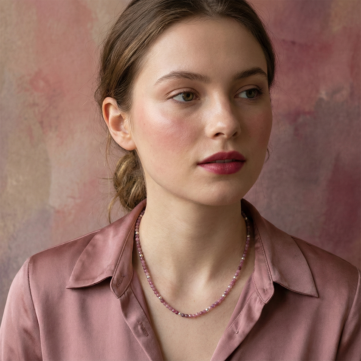 Woman wearing a pink satin shirt and a beaded necklace against a soft pink background