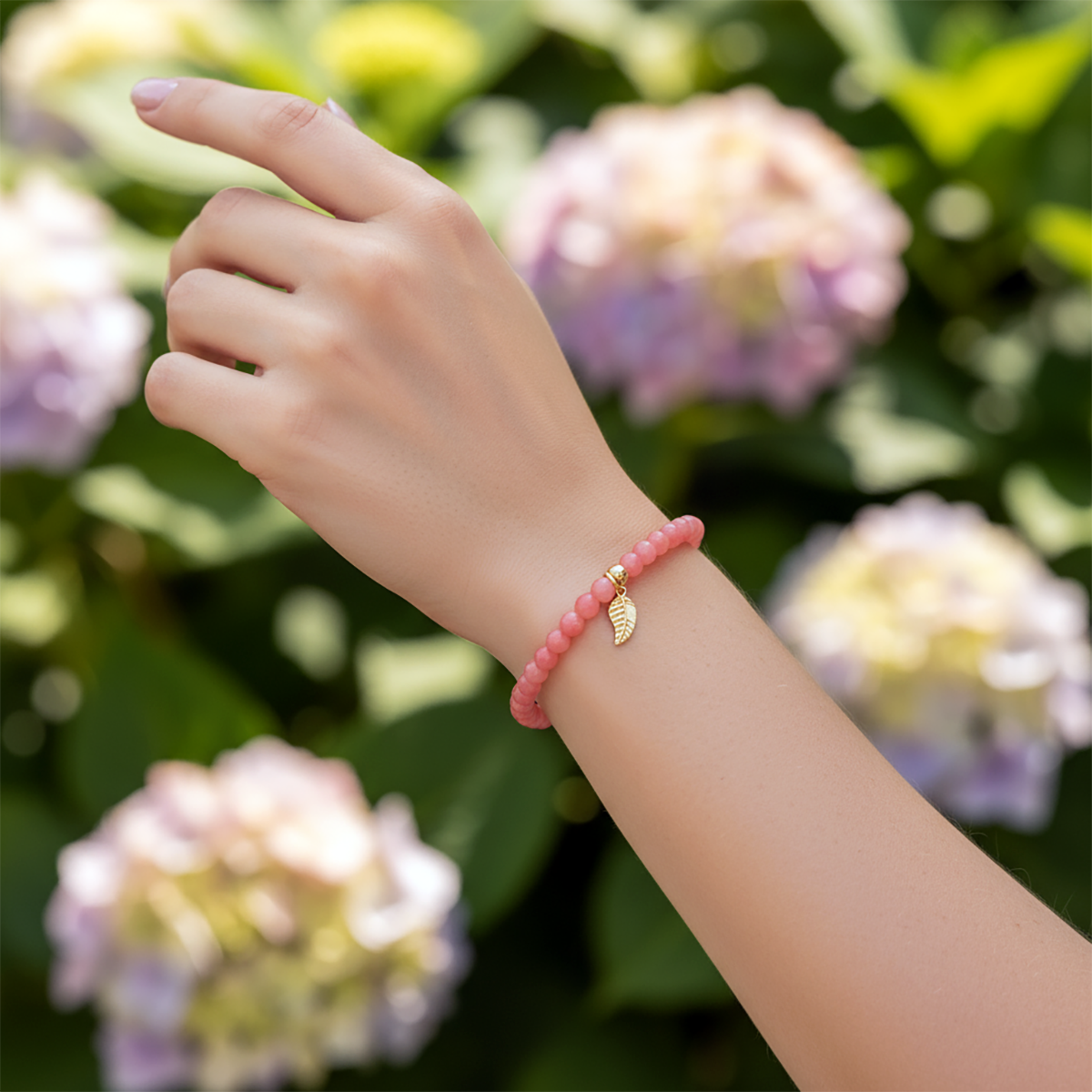 Hand wearing a pink beaded bracelet with a gold leaf charm against a floral background