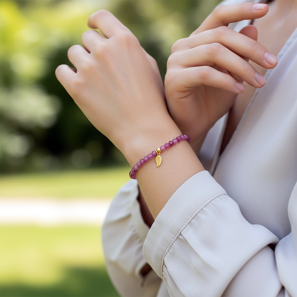 Close-up of a person wearing a pink beaded bracelet with a gold leaf charm, outdoors.