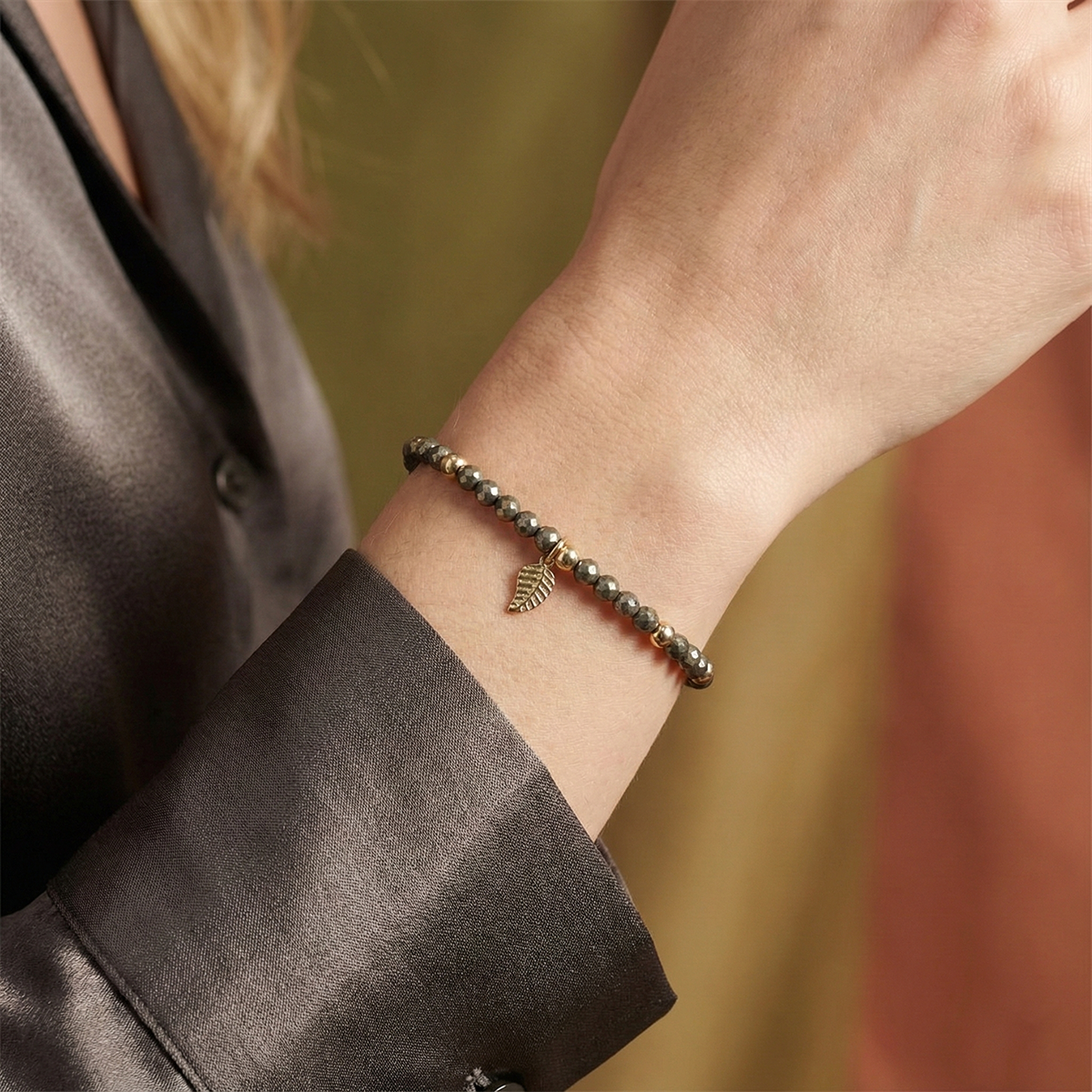 Bracelet with leaf charm on a wrist against a blurred background