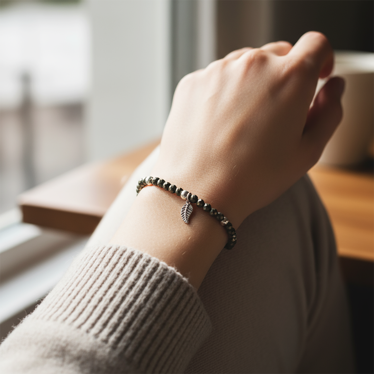 Hand wearing a bracelet with a leaf charm, blurred background
