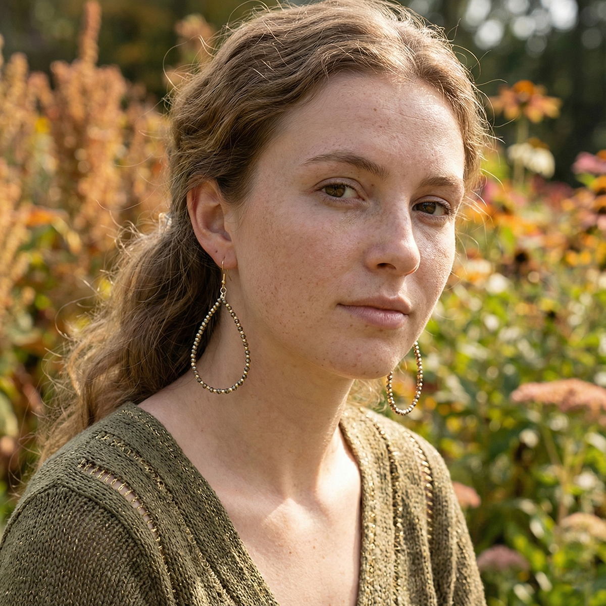 Woman with braided hair and hoop earrings standing in a field of flowers