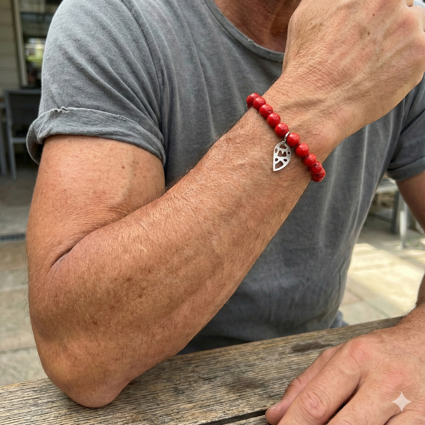 Person wearing a red beaded bracelet with a silver heart charm on an arm.