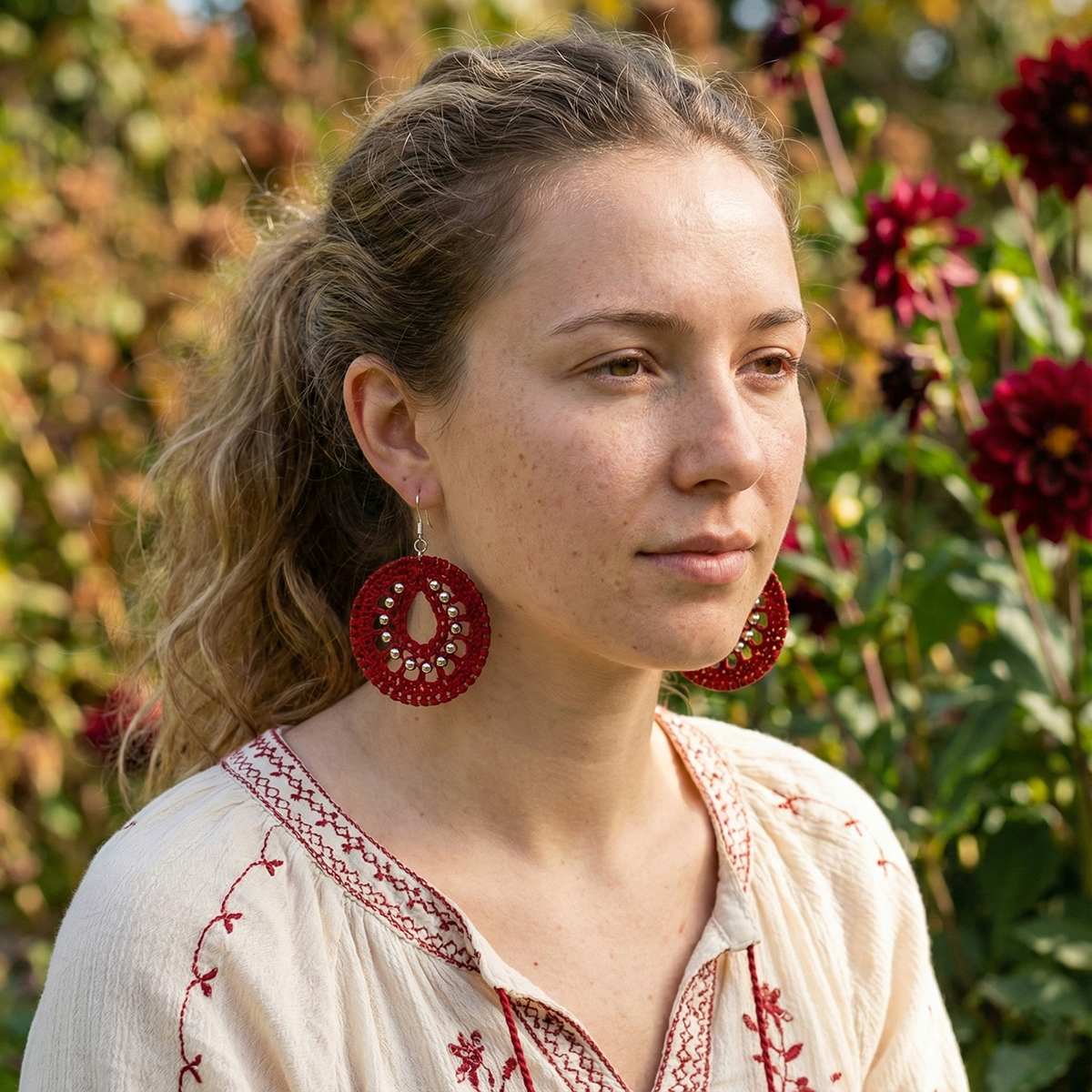 Woman wearing red earrings and a patterned top in a garden setting