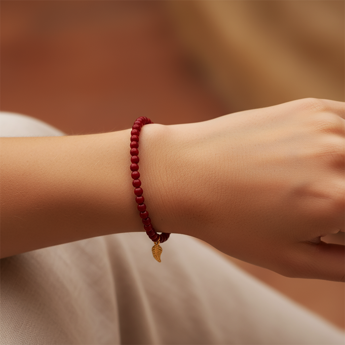 Red beaded bracelet with a gold charm on a wrist against a blurred background