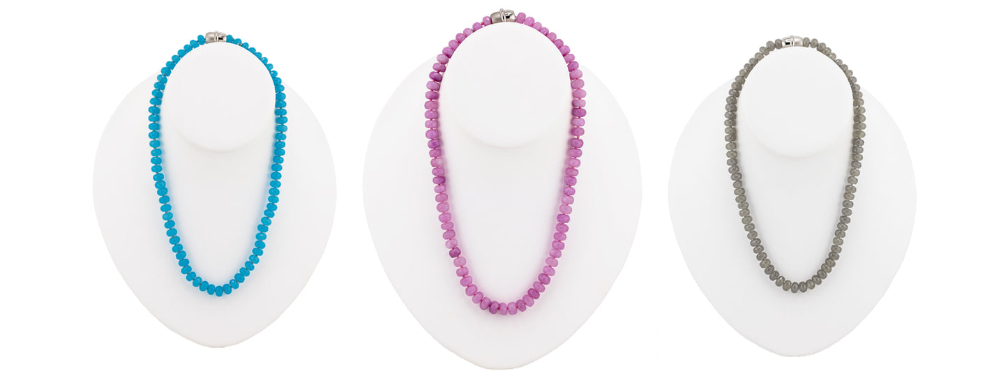 Three beaded necklaces displayed on white mannequin busts against a white background: a turquoise-blue necklace, a pink-purple necklace, and a silver-gray necklace.