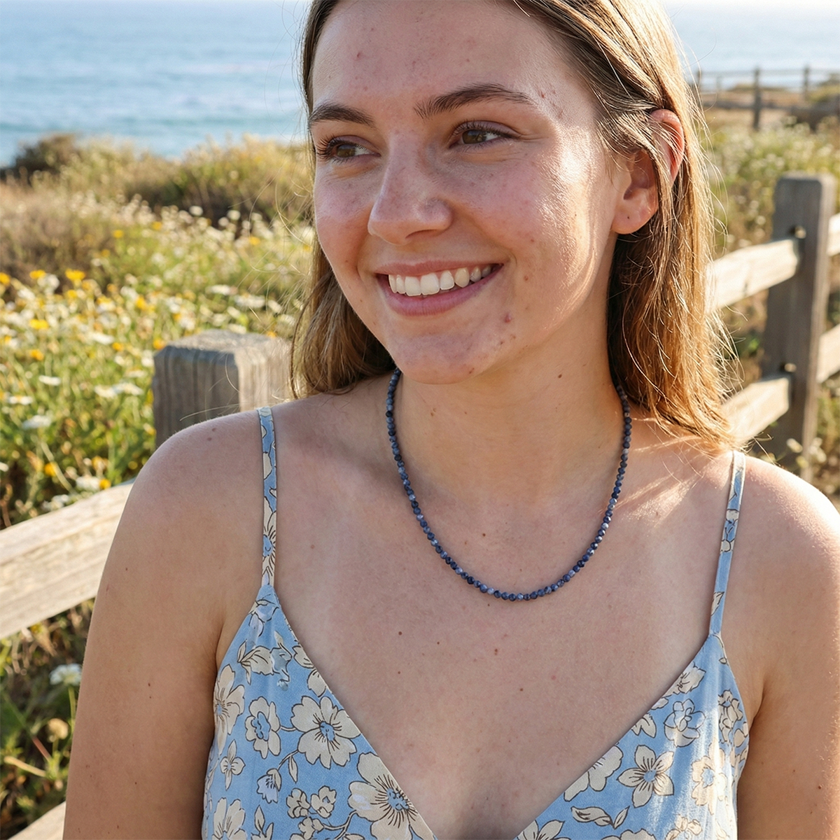 Woman wearing a blue floral dress with a necklace, standing outdoors with a natural background