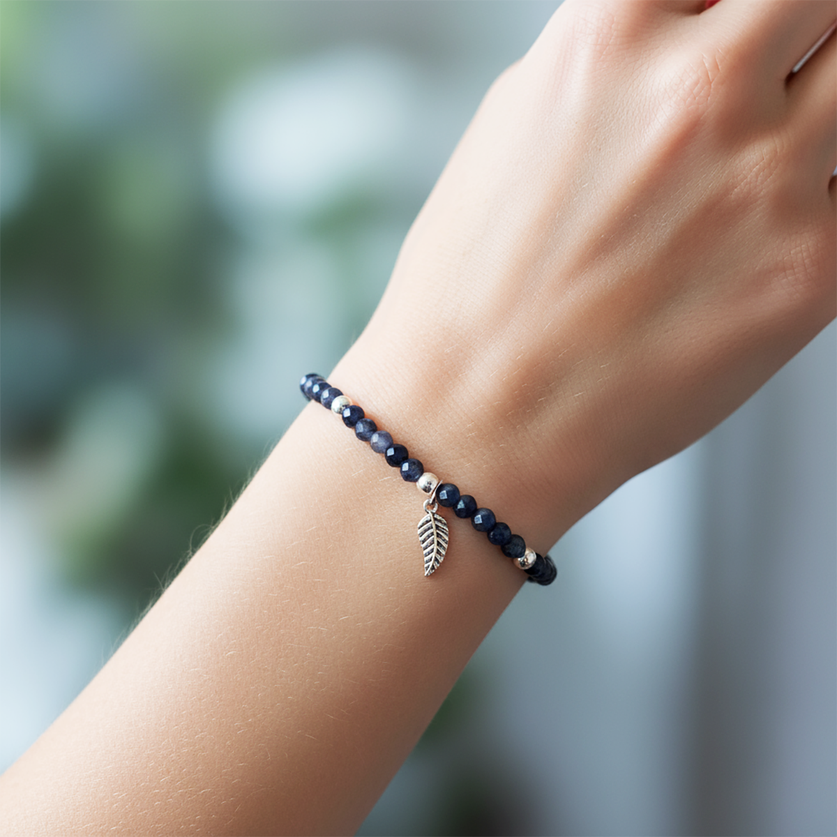 Navy beaded bracelet with a leaf charm on a wrist against a blurred natural background