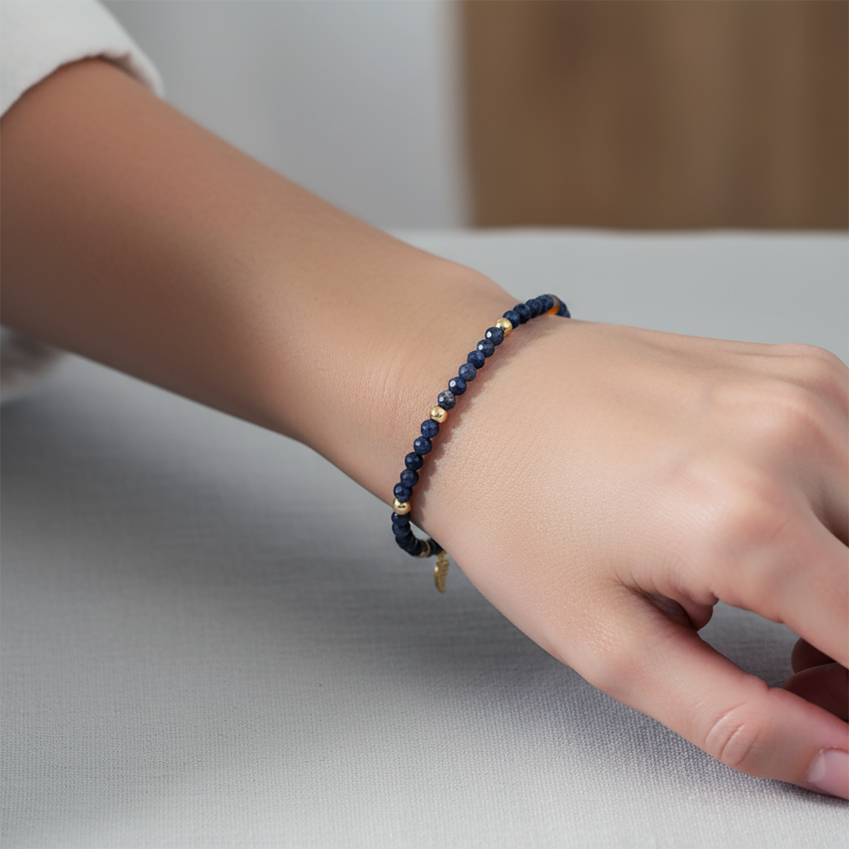 Hand wearing a blue beaded bracelet on a neutral background