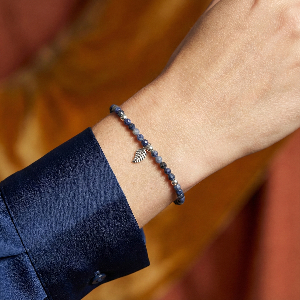 Close-up of a wrist wearing a beaded bracelet with a leaf charm against a blurred background.