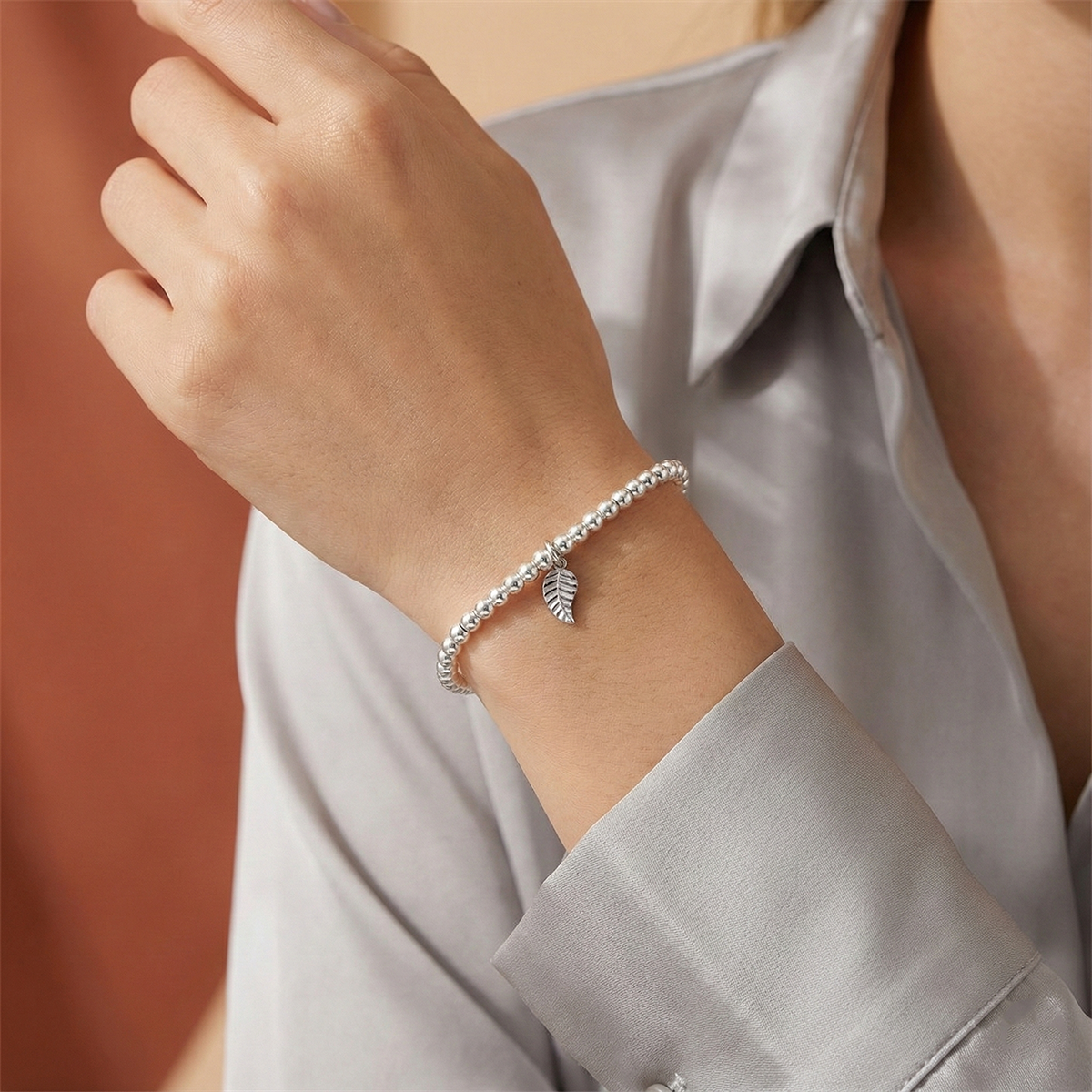 Silver bracelet with leaf charm on a wrist against a neutral background