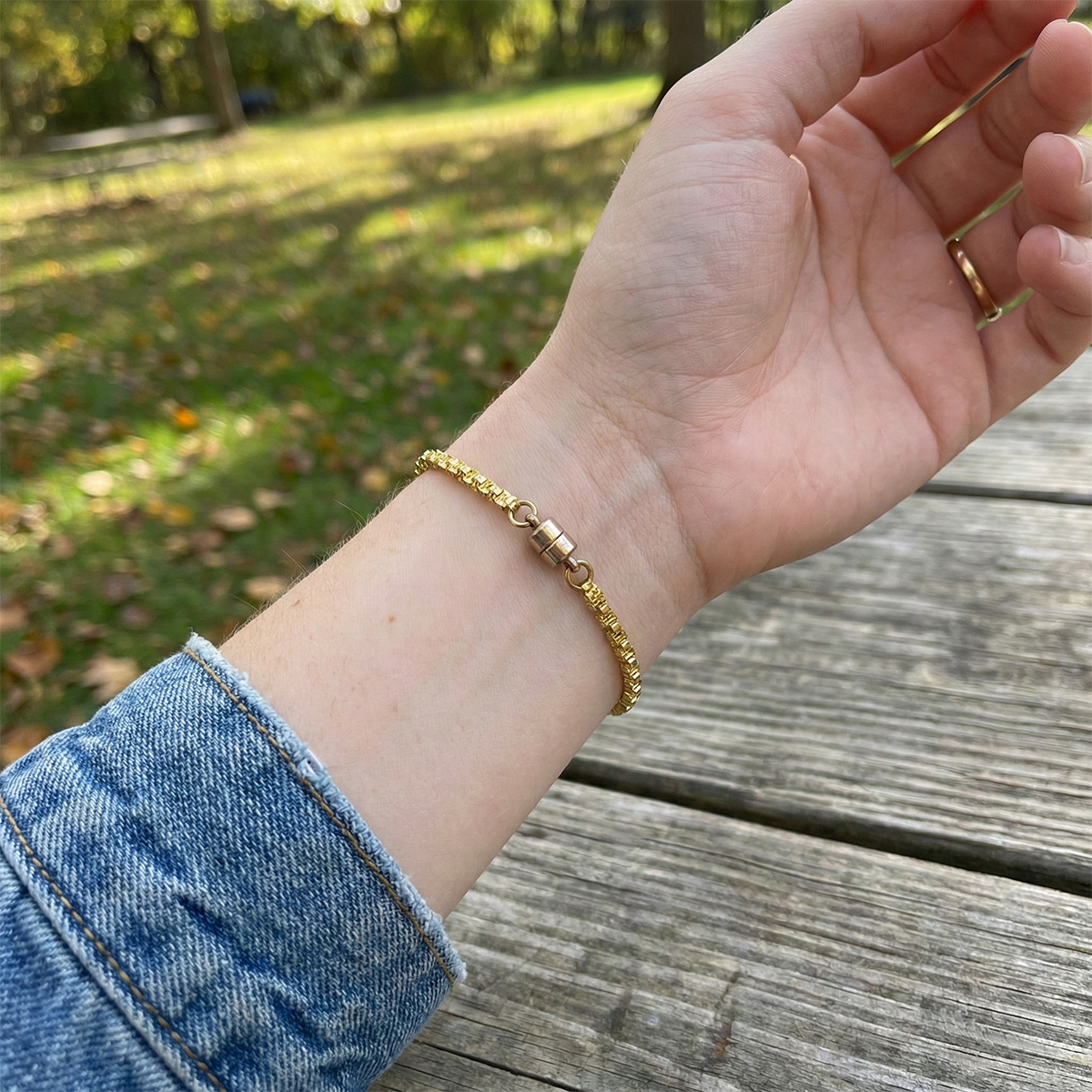 Gold bracelet on a wrist with a blurred outdoor background