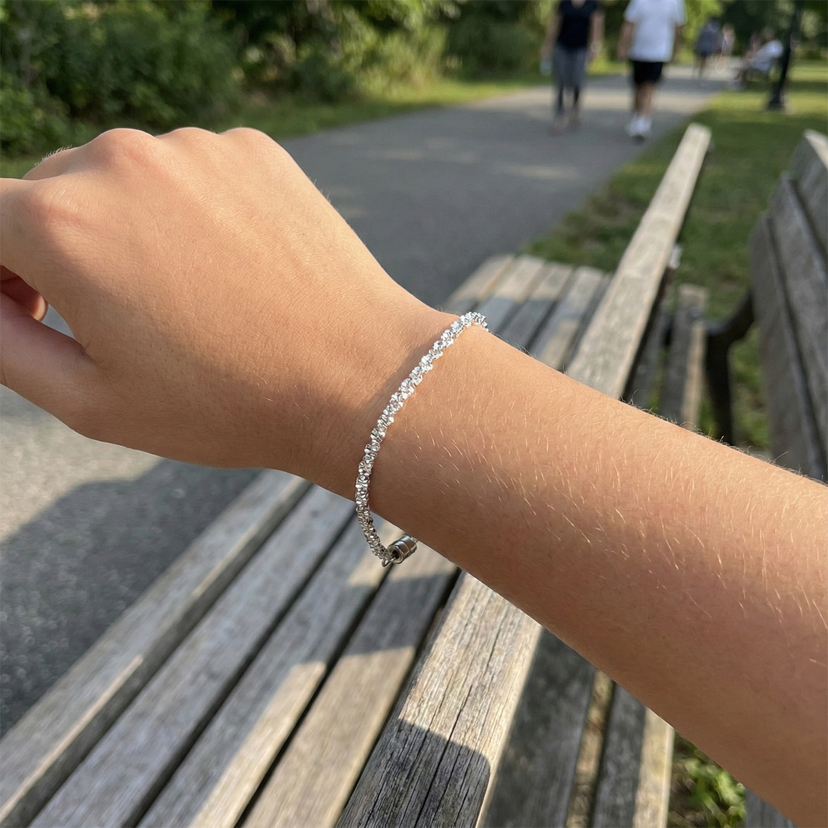 Hand wearing a silver bracelet on a wooden bench with a park background
