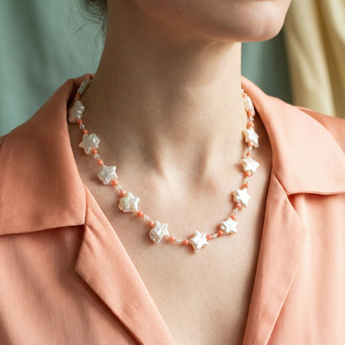 Necklace with star-shaped pearls worn by a person in a peach-colored shirt.