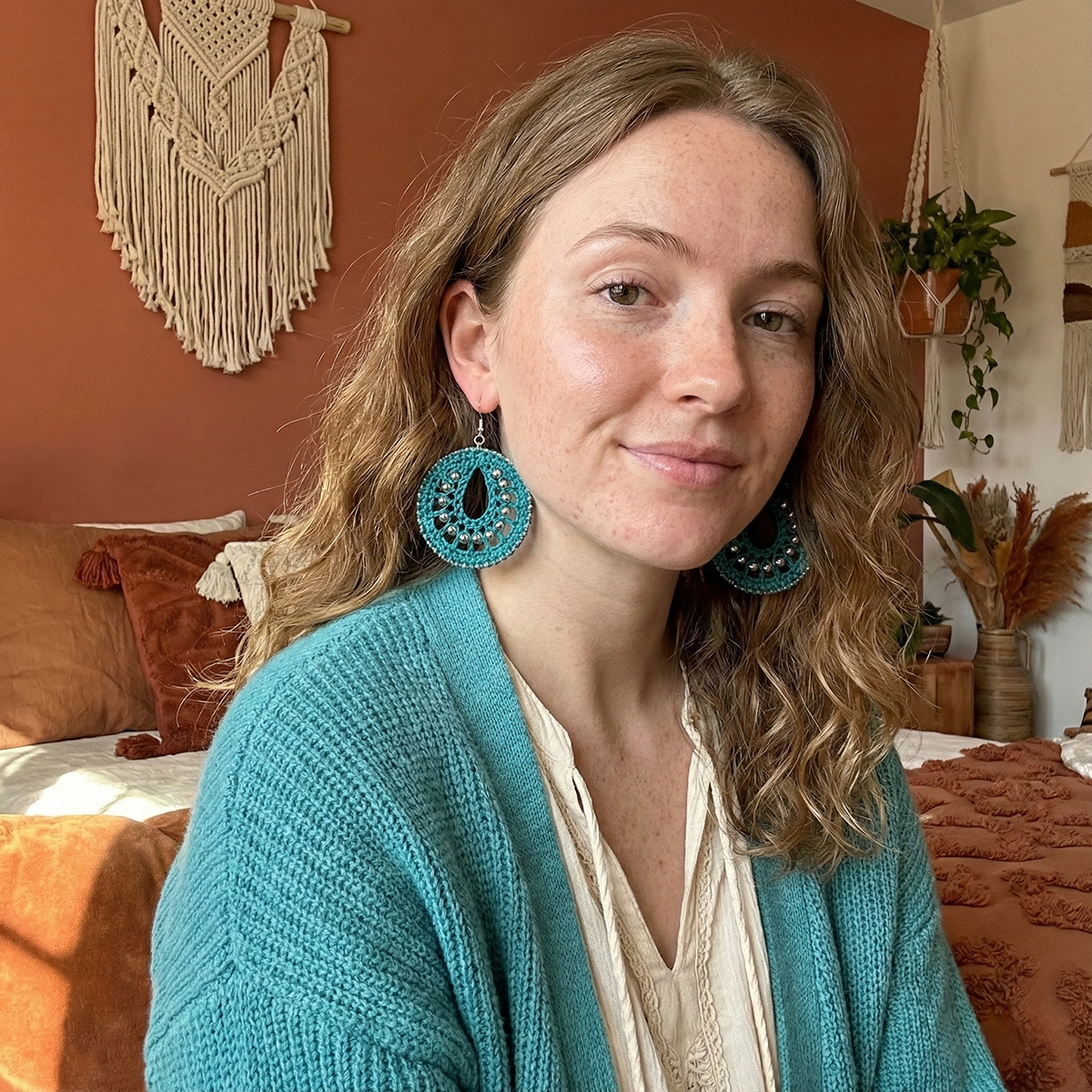 Woman wearing turquoise earrings in a cozy room with decorative elements.