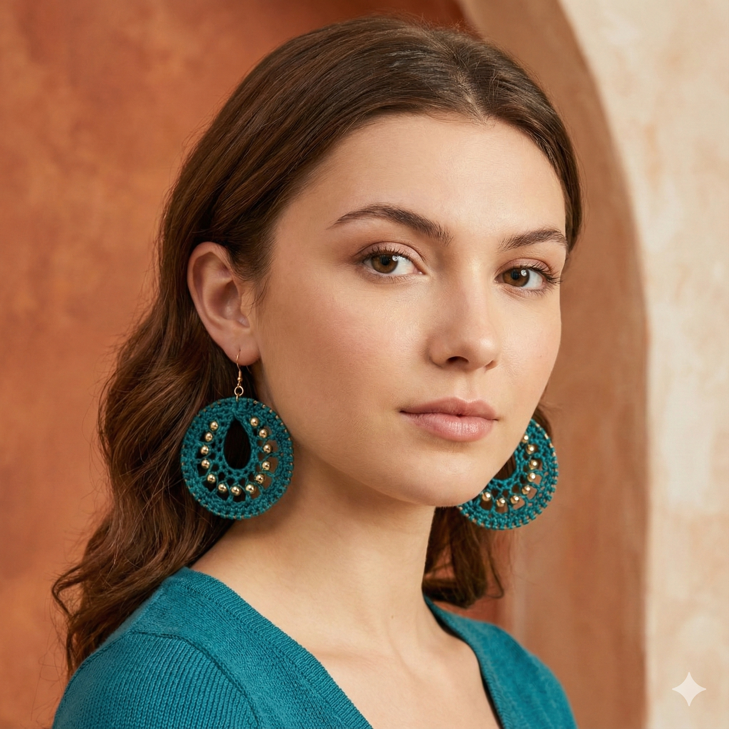 Woman wearing teal earrings against a warm-toned background