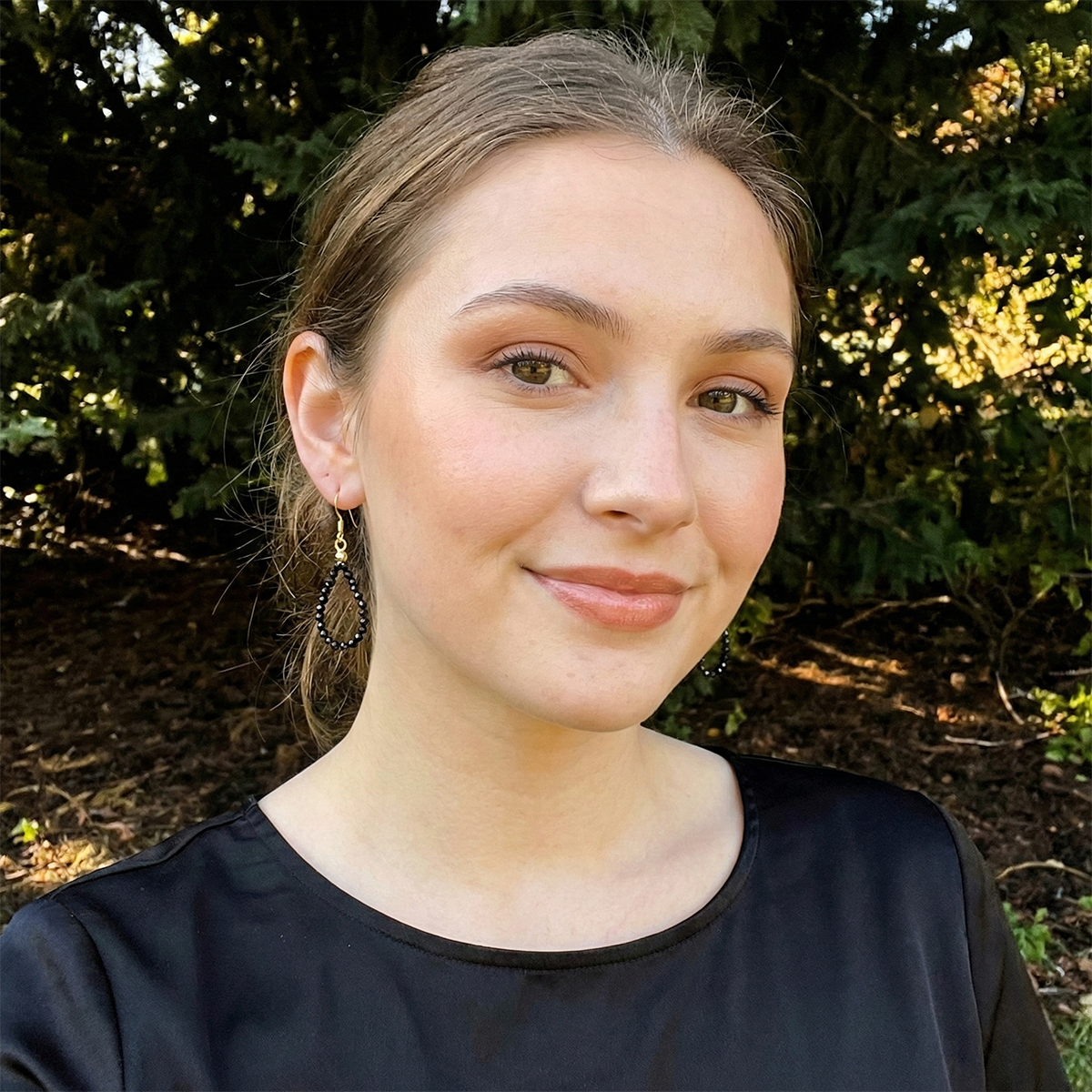 Woman with a black top standing outdoors with greenery in the background