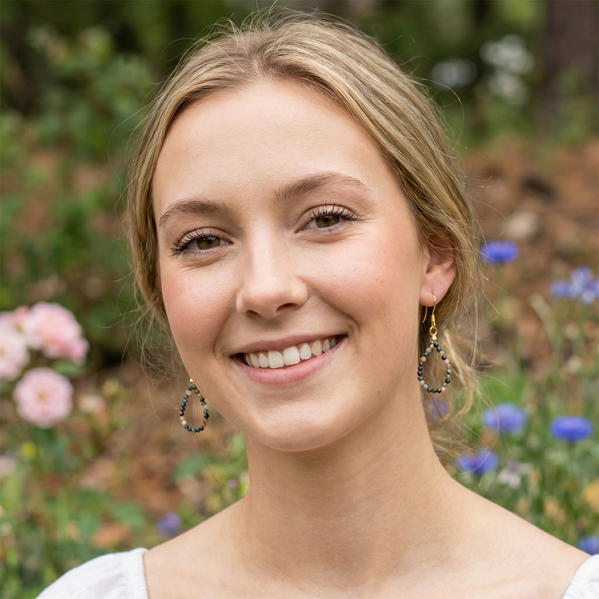 Woman with hoop earrings standing in a garden with flowers