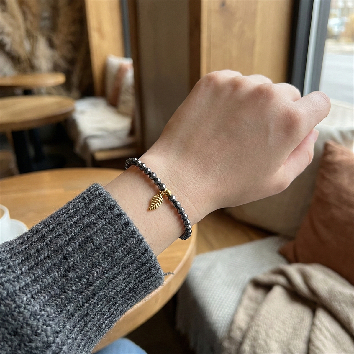 Hand wearing a bracelet with a leaf charm in a cozy indoor setting