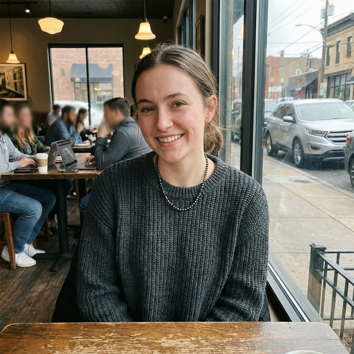 Woman sitting at a cafe smiling with a city street view outside