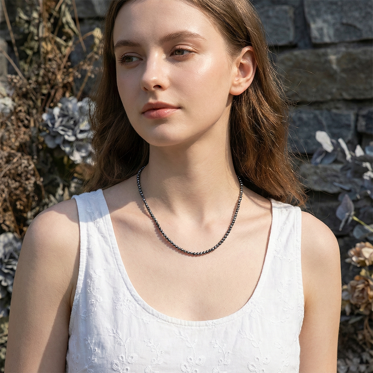 Woman wearing a necklace with a stone wall and plants in the background