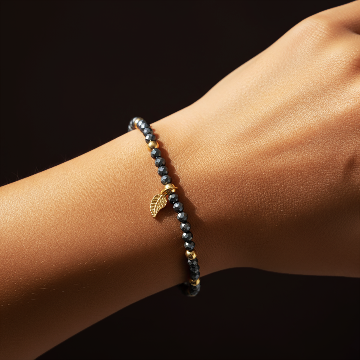 Bracelet with leaf charm on a wrist against a black background