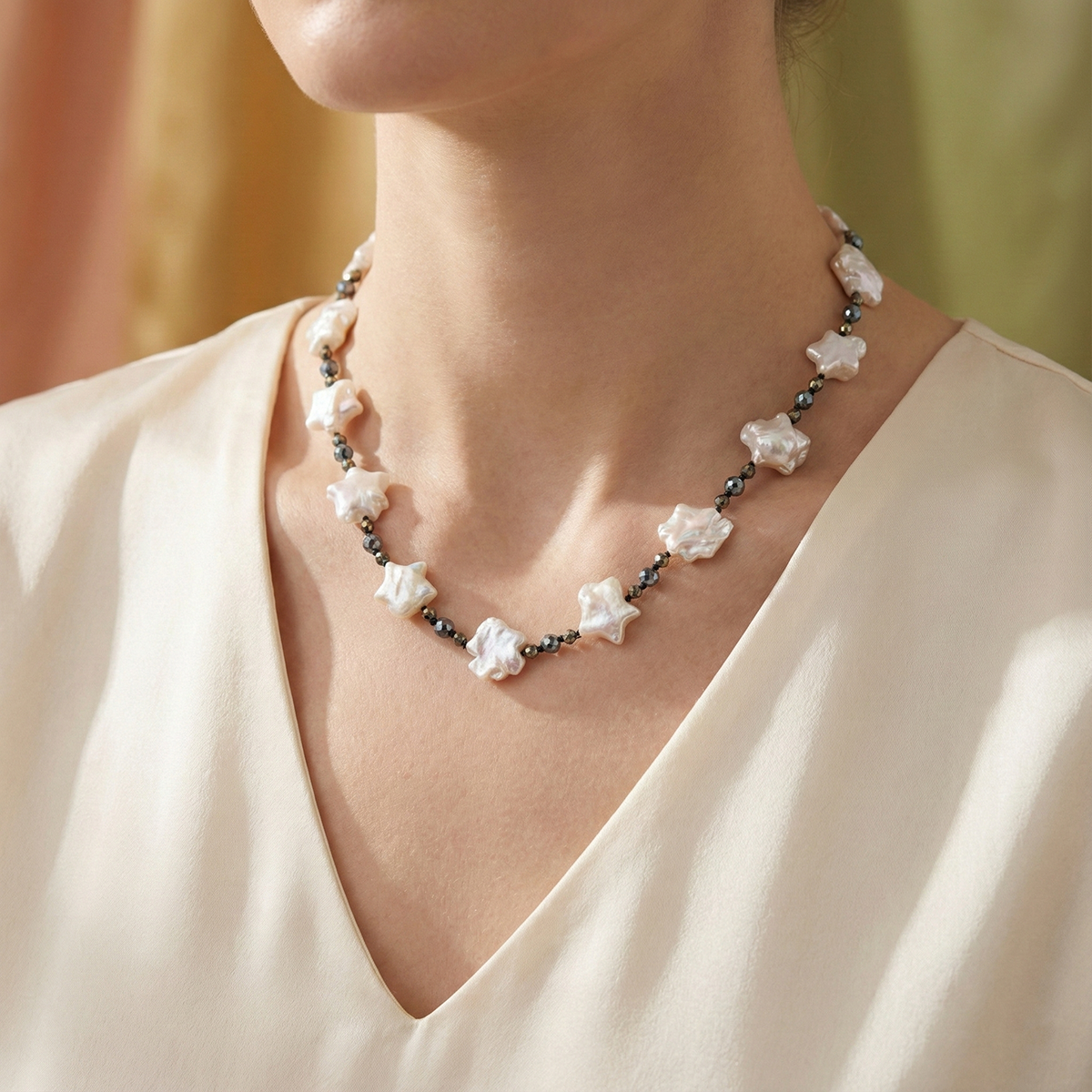 Necklace with star-shaped pearls worn by a person in a cream-colored top.