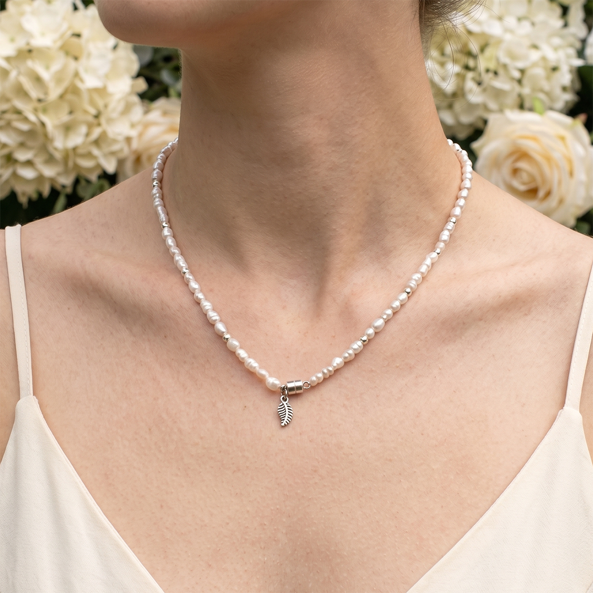 Pearl necklace with a silver pendant worn by a person against a floral background