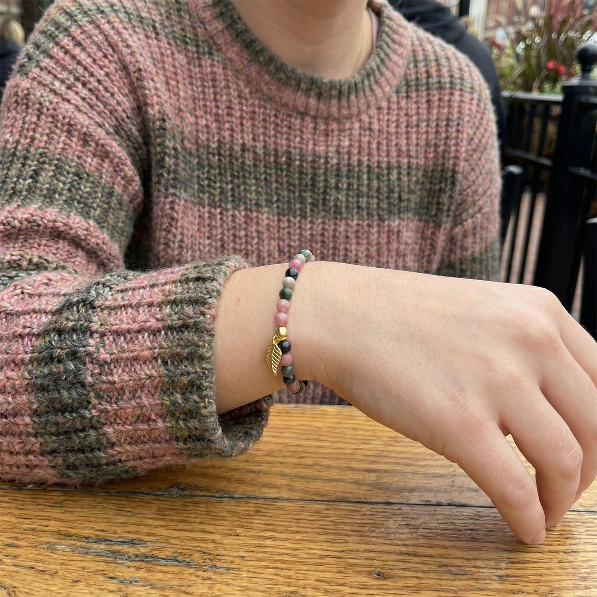 Person wearing a bracelet with a pink sweater on a wooden table